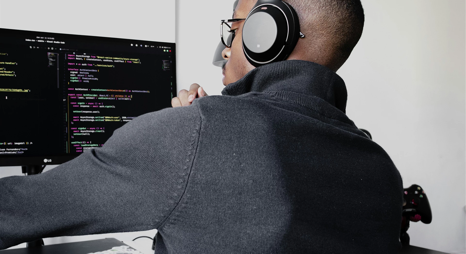 A developer wearing headphones works on code displayed on a monitor screen.