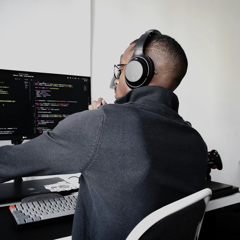 Un développeur porte un casque d'écoute et travaille sur du code affiché sur un écran d'ordinateur.